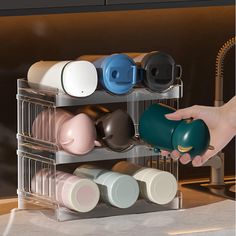 a person holding a coffee cup in front of a metal rack with cups on it