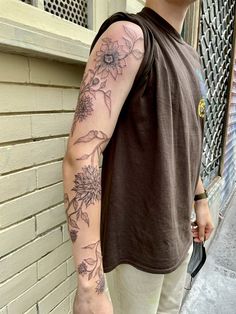 a man with a flower tattoo on his arm standing next to a building and holding an umbrella