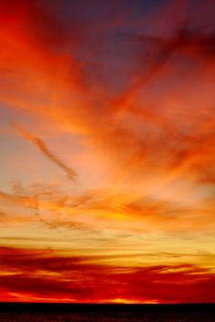 the sky is red and orange as it sets over the ocean with an airplane flying in the distance