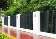 a white fence with black iron bars on the top and bottom is next to a red brick sidewalk