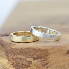 two gold wedding rings sitting on top of a wooden table next to each other,