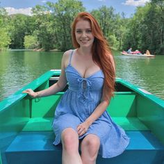 a woman in a blue dress is sitting on a green boat and smiling at the camera