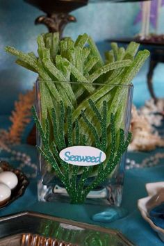 a glass vase filled with green plants on top of a blue cloth covered tablecloth