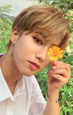 a person holding a flower in front of their face and looking at the camera with one hand