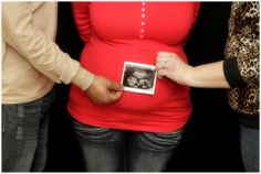 a pregnant woman holding a baby photo in front of her belly while standing next to two other people