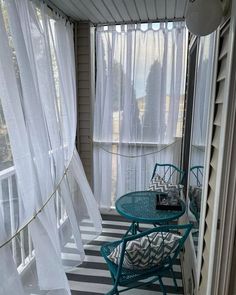 two chairs and a table in front of a window with sheer curtains on the outside