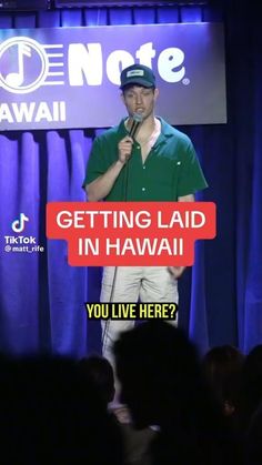 a man holding a microphone while standing in front of a sign that says getting laid in hawaii you live here?