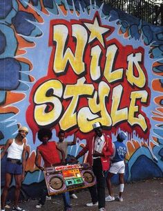 four people standing in front of a graffiti wall with the words wild's style on it