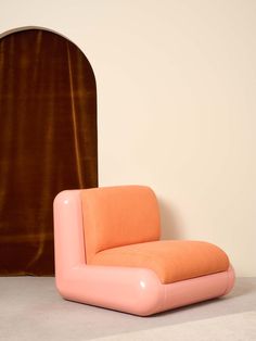 an orange and pink chair sitting in front of a brown wall with a curtain behind it