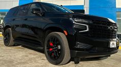 a black chevrolet suv parked in front of a blue and white building with the door open