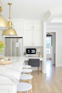 a kitchen with white cabinets and marble counter tops, gold pendant lights over the island