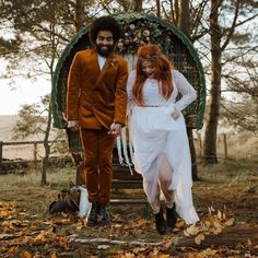 a man and woman dressed up in wedding attire walking through the woods with leaves on the ground