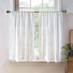 a window with white curtains in front of it and a potted plant next to the window