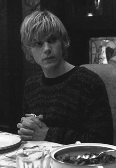 a young man sitting at a table with his hands clasped