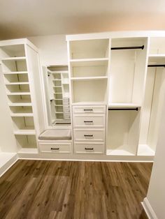 an empty walk in closet with wooden floors and white cabinets on the wall, along with open shelving units