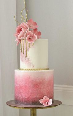 a three tiered cake with pink flowers on the top and gold trimmings