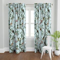 a white chair sitting in front of a window covered in blue curtain panels with birds on them