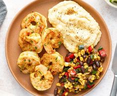 a plate with shrimp, mashed potatoes, corn and black beans on it next to a fork