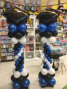 two graduation balloons in the shape of columns with black, white and blue balloons attached to them