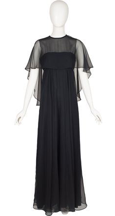 "This 1970s Jean Varon floor length evening dress was made in England of a lined black polyester chiffon. As with all classic Jean Varon, it was designed by John Bates. It features an empire waist and a built-in chiffon overlay with tassels at the back. It does up the back with a YKK zipper and a button at the back of the neck. It's in excellent, ready-to-wear condition. Measurements: Bust - 35\" Empire waist - 29\" Hips - 38\" Length - 61\" IMPORTANT NOTE FOR CANADIAN SHOPPERS: There is a 15% s Formal Black Silk Chiffon Maxi Dress, Black Silk Chiffon Maxi Evening Dress, Evening Sheer Dress With Cape Sleeves, Chiffon Maxi Dress With Cape Sleeves For Evening, Black Silk Chiffon Evening Dress For Formal Occasions, Black Silk Chiffon Evening Dress For Gala, Sheer Silk Chiffon Maxi Dress For Evening, Black Silk Chiffon Party Maxi Dress, Black Silk Chiffon Evening Dress For Party