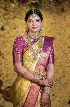 a woman wearing a yellow and pink sari with gold jewelry on her neck, standing in