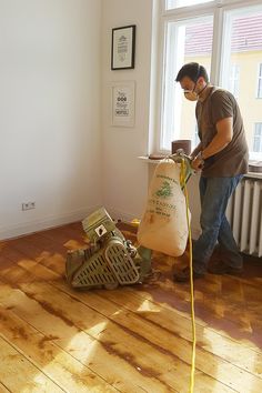 a man is sanding the wood floor with a vacuum and duster in his hand