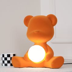 an orange teddy bear lamp sitting on top of a table next to a black and white checkered wall