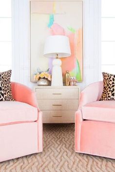 a living room with two pink chairs and a painting on the wall behind them,