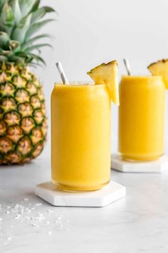 two glasses filled with pineapple smoothie next to a pineapple on the side