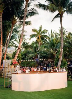 an outdoor bar with palm trees in the background and people sitting at tables behind it