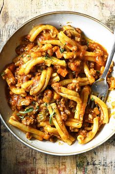 pasta with meat and sauce in a bowl on a wooden table next to a fork