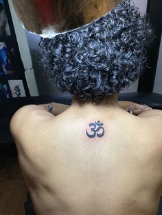 the back of a woman's head with a tattoo on her upper half and an om symbol behind it