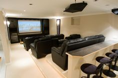 a large home theater with black chairs and a bar in front of the television screen