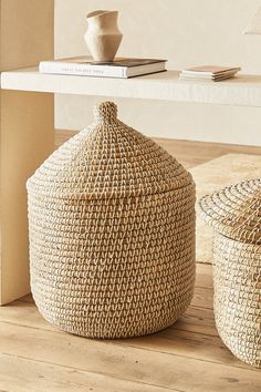 two woven storage baskets sitting on top of a wooden floor next to a white table