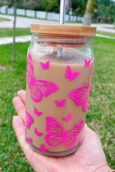 a hand holding a jar with pink butterflies painted on the side and a straw in it