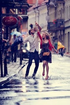 a man and woman are dancing in the rain on a city street with umbrellas