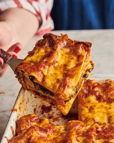 a person cutting into some lasagna casserole on a plate with a spatula