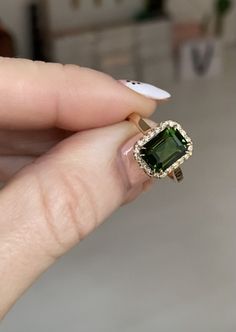 a woman's hand holding an emerald and diamond ring