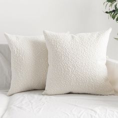 two white pillows sitting on top of a bed next to a green potted plant