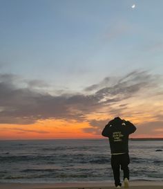 a man standing on top of a sandy beach next to the ocean at sunset or dawn