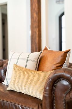 a brown leather couch with two pillows on it and a mirror in the back ground