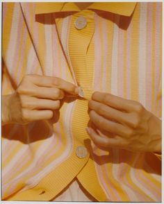 a woman wearing a yellow and white striped shirt is pulling on her tie with both hands