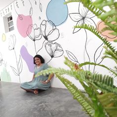 a woman sitting on the ground in front of a wall with flowers painted on it