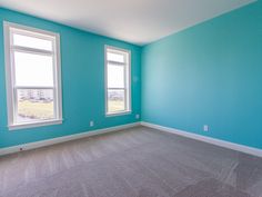 an empty room with blue walls and carpeted floor, two windows in the corner