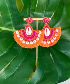 Introducing our "Finding Shells" Earrings in Orange/Fuchsia, a delightful addition to your summer accessory collection. These earrings feature small sea shells beautifully adorned with vibrant orange and fuchsia beads, creating a charming and beachy look. Crafted in a teardrop tassel style, they offer a playful and elegant aesthetic. With a secure post closure and measuring 2.75 inches, they are both stylish and comfortable to wear. Add a touch of seaside charm to your outfit with the "Finding Shells" Earrings in Orange/Fuchsia, perfect for embracing the spirit of summer! Orange Drop Earrings For The Beach, Orange Drop Earrings For Beach, Orange Dangle Jewelry For Beach, Pink Jewelry For Beach Season Vacation, Pink Jewelry For Vacation And Beach Season, Pink Shell-shaped Summer Jewelry, Pink Shell-shaped Jewelry For Summer, Handmade Orange Beaded Earrings For Summer, Pink Dangle Earrings For Summer