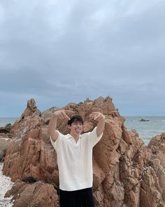 a man standing in front of rocks on the beach with his arms up and smiling