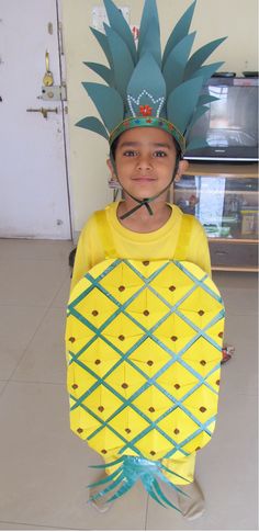 a young boy wearing a pineapple costume with a green crown on his head and blue ribbon around the neck