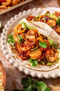 shrimp tacos with guacamole and cilantro on a white plate