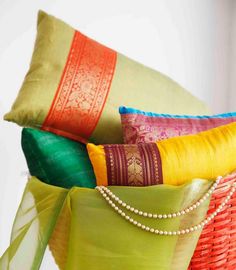 colorful pillows are stacked on top of each other in different colors and patterns, along with a beaded necklace