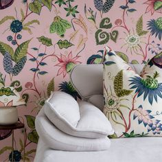 a white couch with pillows on top of it in front of a pink wallpaper